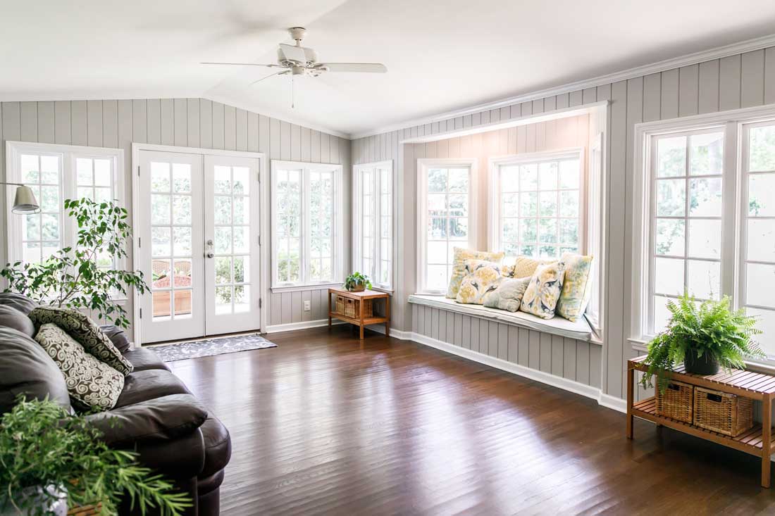 Den with wood flooring, gray couch, ceiling fan, window, pillows, and indoor plants