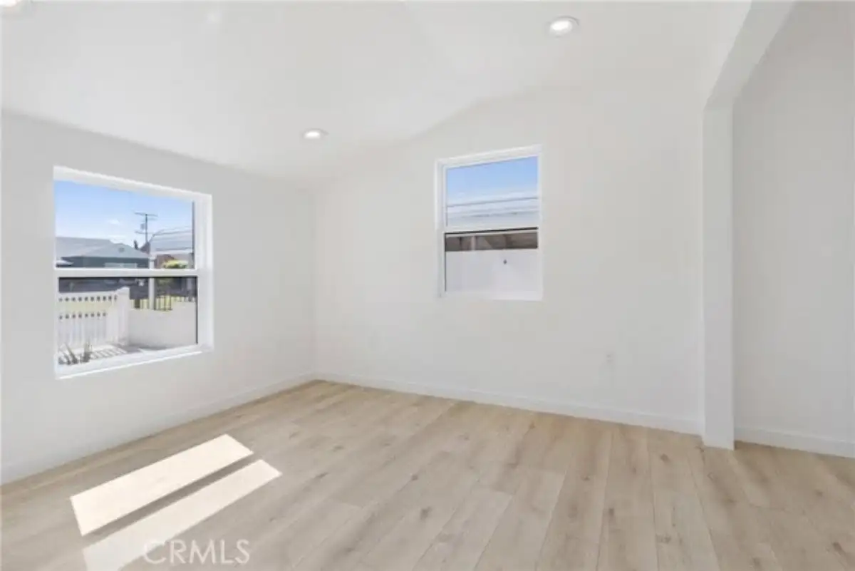 Empty bedroom with wood flooring, two windows, and white walls